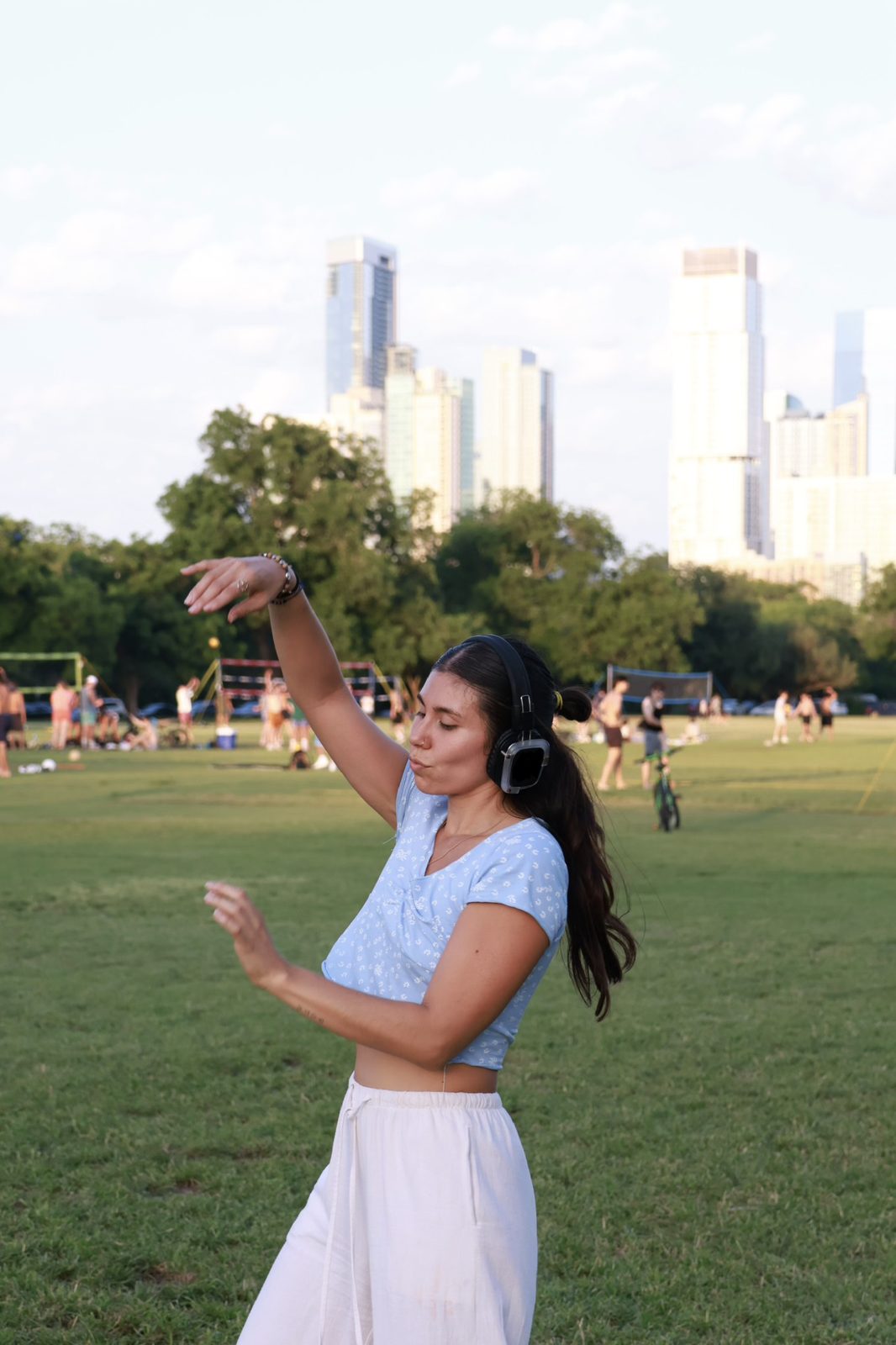 Maria dancing with headphones in an Austin park with the skyline behind her