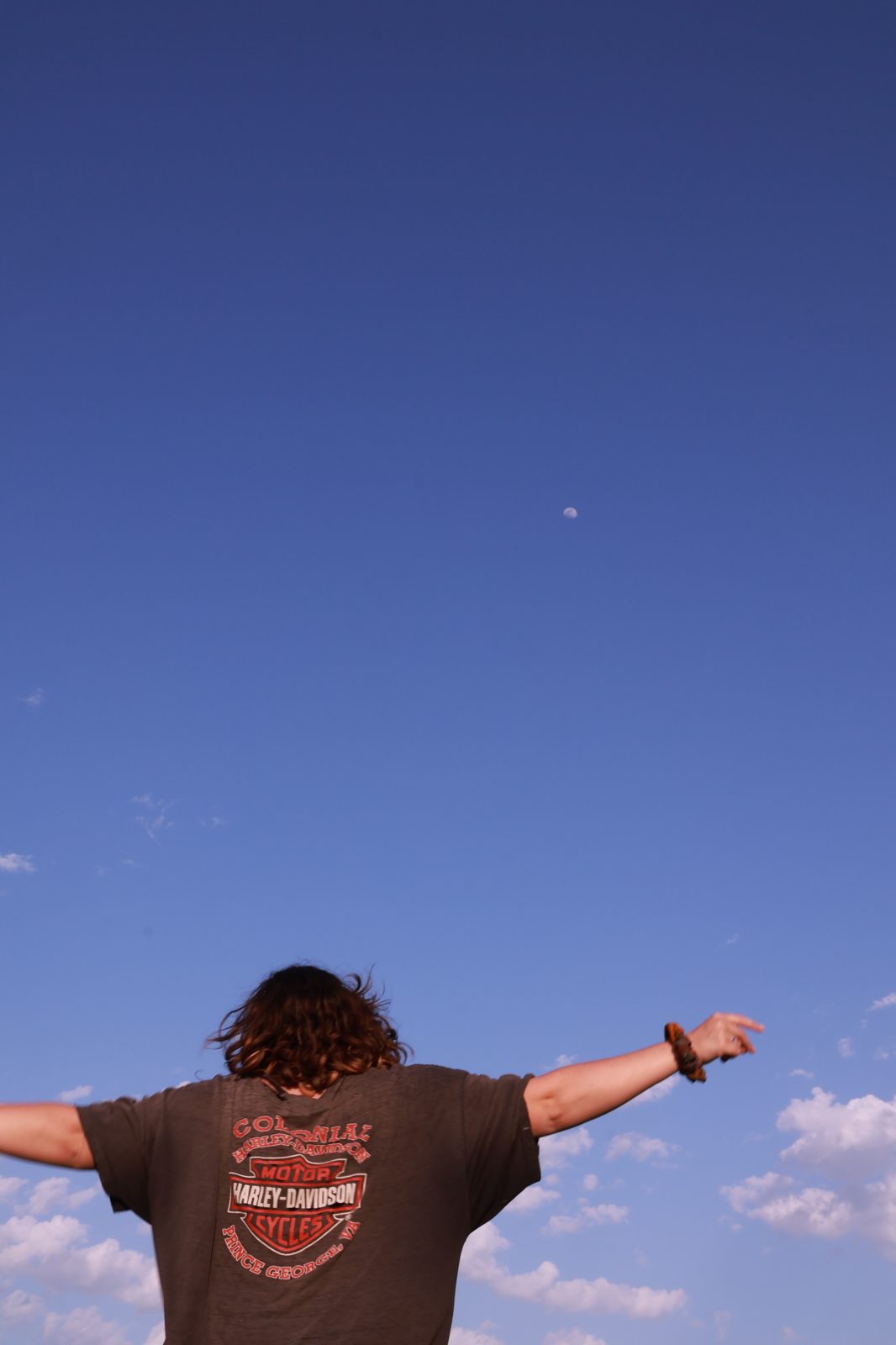 Reilley with arms outstretched toward the sky and moon at a park silent disco